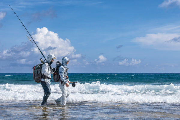 Two guys walking the shore edge wearing simms solarflex hoodys looking for fish